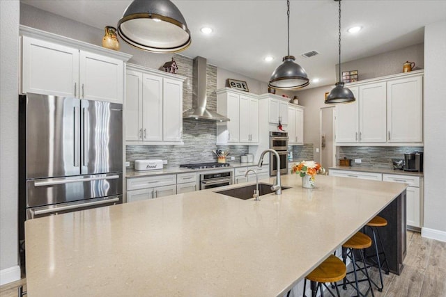 202 Iron Rail Ln, Georgetown, TX 78633 - kitchen with wall chimney range hood, stainless steel appliances, a large island with sink, light wood-style flooring, and white cabinetry