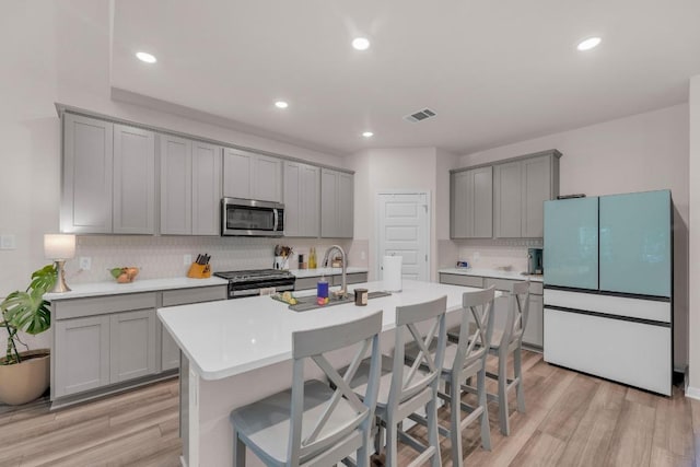 133 Fairmeadow Downs Dr, Hutto, TX 78634 - kitchen featuring stainless steel microwave, freestanding refrigerator, gray cabinets, tasteful backsplash, and gas stove