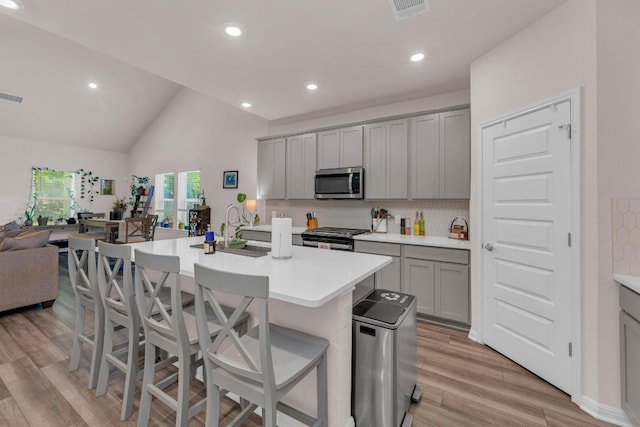 133 Fairmeadow Downs Dr, Hutto, TX 78634 - kitchen featuring stainless steel microwave, gray cabinets, light wood-type flooring, vaulted ceiling, and light countertops