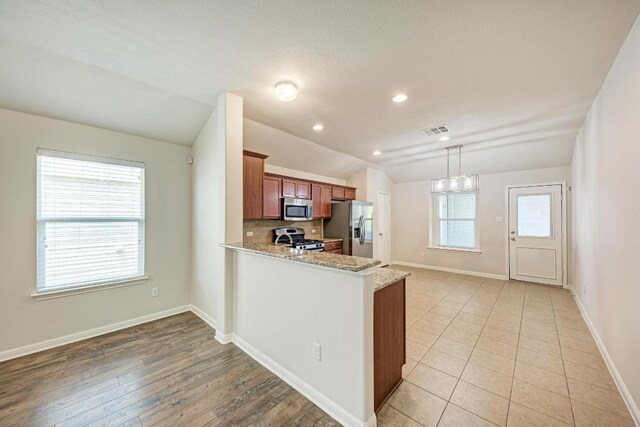 486 Nottingham Loop, Kyle, TX 78640 - kitchen with appliances with stainless steel finishes, brown cabinets, lofted ceiling, a peninsula, and light stone countertops