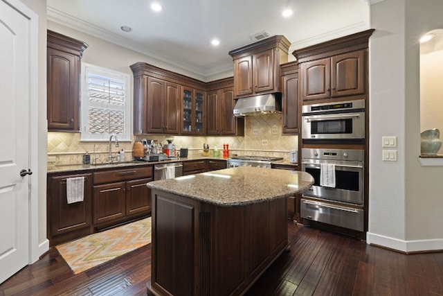 1036 Liberty Park Dr Unit 46, Austin, TX 78746 - kitchen with a warming drawer, under cabinet range hood, ornamental molding, dark stone counters, and dark wood-style floors