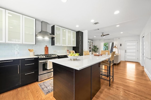 1010 Karen Ave, Austin, TX 78757 - kitchen with stainless steel gas range, wall chimney exhaust hood, a kitchen breakfast bar, light countertops, and tasteful backsplash