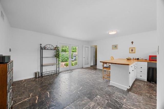 1209 Clearfield Dr, Austin, TX 78758 - kitchen featuring white cabinets, a peninsula, a kitchen bar, dark marble finish flooring, and wood counters