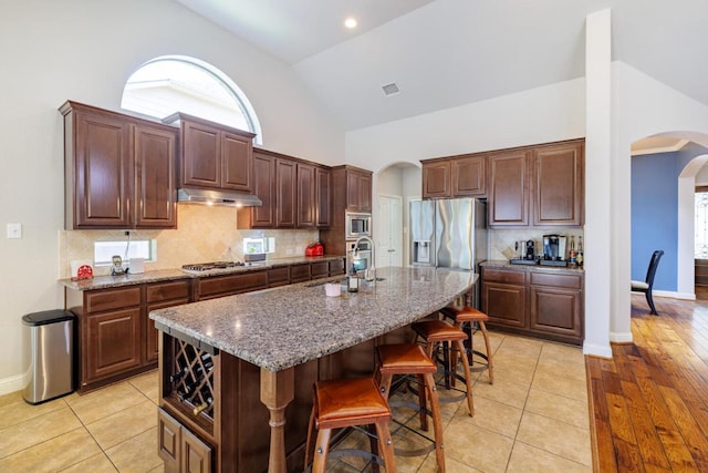 2843 Nolina Ln, Round Rock, TX 78681 - kitchen featuring arched walkways, high vaulted ceiling, a kitchen breakfast bar, stainless steel appliances, and an island with sink