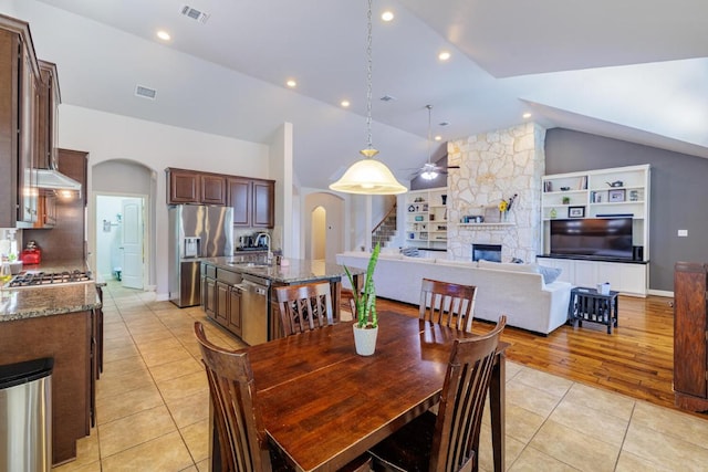 2843 Nolina Ln, Round Rock, TX 78681 - dining space with arched walkways, light tile patterned flooring, vaulted ceiling, a stone fireplace, and built in features