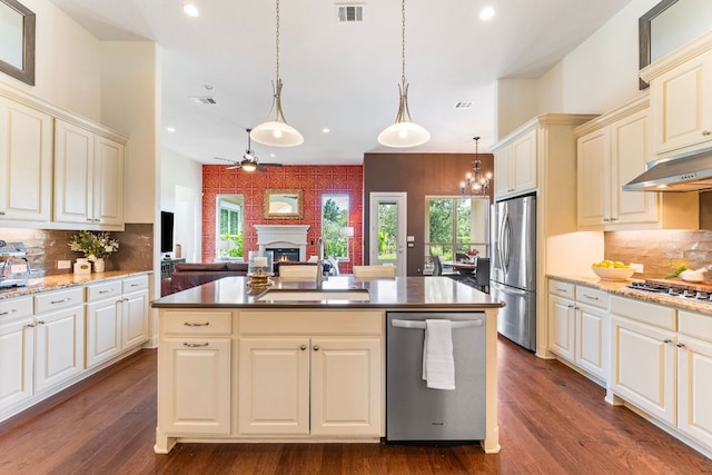 1821 Gilded Crest Dr, Leander, TX 78641 - kitchen featuring appliances with stainless steel finishes, cream cabinetry, a lit fireplace, under cabinet range hood, and recessed lighting
