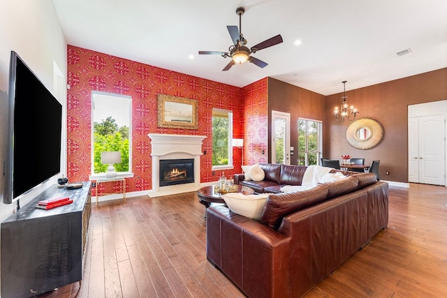 1821 Gilded Crest Dr, Leander, TX 78641 - living room featuring wallpapered walls, a chandelier, a warm lit fireplace, ceiling fan, and hardwood / wood-style flooring