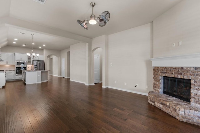 7901 Arbor Knoll Ct, Lago Vista, TX 78645 - unfurnished living room with arched walkways, a chandelier, a glass covered fireplace, dark wood finished floors, and lofted ceiling