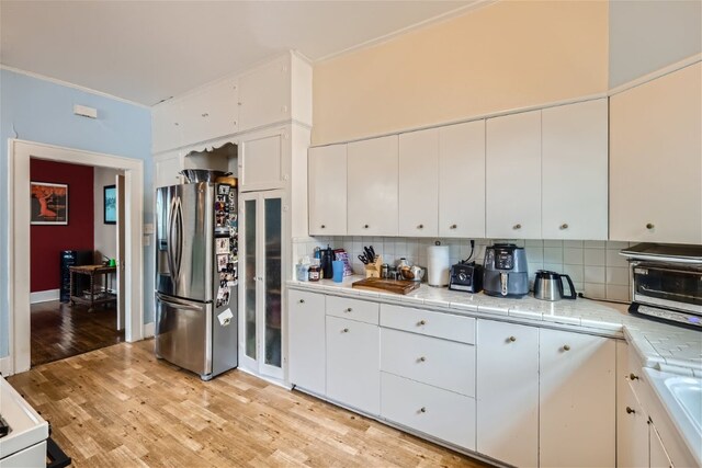 1508 Pease Rd, Austin, TX 78703 - kitchen featuring stainless steel fridge with ice dispenser, decorative backsplash, light wood finished floors, white cabinets, and ornamental molding