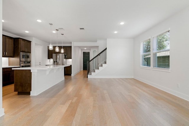 265 Tierra Trl, Dripping Springs, TX 78620 - kitchen with stainless steel appliances, light countertops, dark brown cabinetry, light wood-style flooring, and an island with sink