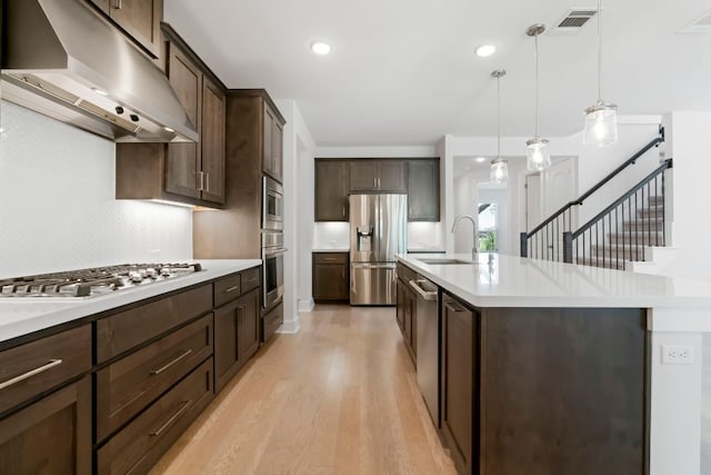 265 Tierra Trl, Dripping Springs, TX 78620 - kitchen featuring extractor fan, stainless steel appliances, dark brown cabinetry, a center island with sink, and light wood-style floors