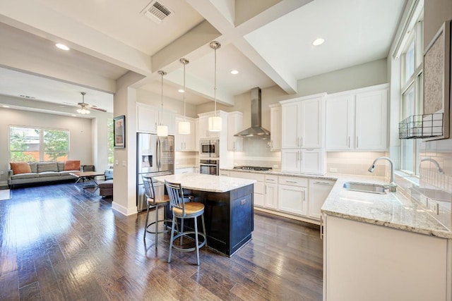 3105 Mccurdy St, Austin, TX 78723 - kitchen featuring stainless steel appliances, wall chimney range hood, a kitchen island, white cabinets, and light stone counters