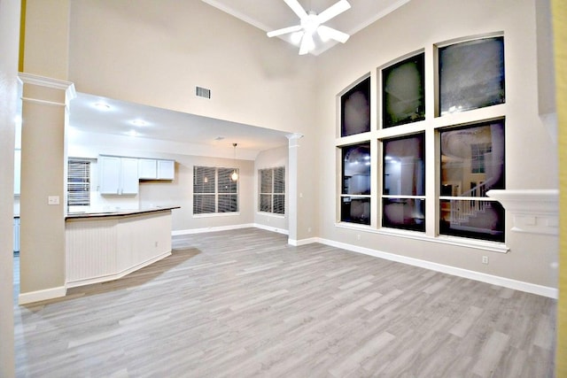 1933 Chasewood Dr, Austin, TX 78727 - unfurnished living room with a ceiling fan, light wood-type flooring, ornate columns, a towering ceiling, and crown molding