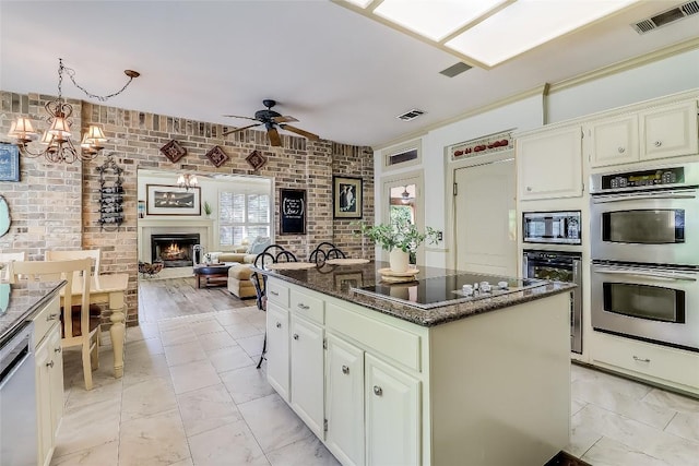 3110 Barton Point Dr, Austin, TX 78733 - kitchen with stainless steel appliances, a warm lit fireplace, a kitchen island, brick wall, and a ceiling fan