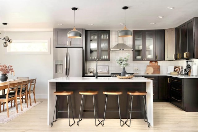 5806 Burnhill Dr, Austin, TX 78745 - kitchen with stainless steel refrigerator with ice dispenser, wall chimney range hood, light wood-style floors, a kitchen bar, and recessed lighting