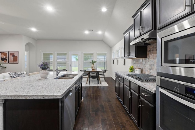 19825 Rhiannon Ln, Pflugerville, TX 78660 - kitchen featuring stainless steel appliances, under cabinet range hood, dark wood finished floors, arched walkways, and tasteful backsplash