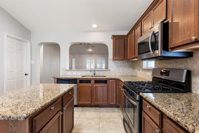 1704 Big Bend Dr, Cedar Park, TX 78613 - kitchen featuring appliances with stainless steel finishes, backsplash, arched walkways, light stone countertops, and a center island