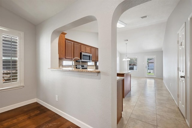 1704 Big Bend Dr, Cedar Park, TX 78613 - kitchen with stainless steel microwave, arched walkways, brown cabinets, lofted ceiling, and a peninsula