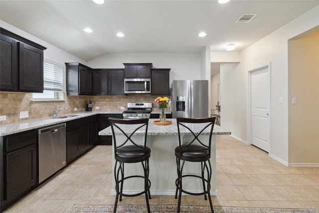132 Sage Meadows Dr, San Marcos, TX 78666 - kitchen featuring appliances with stainless steel finishes, decorative backsplash, light stone counters, light tile patterned floors, and a breakfast bar