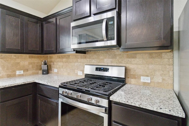 132 Sage Meadows Dr, San Marcos, TX 78666 - kitchen featuring appliances with stainless steel finishes, dark brown cabinetry, backsplash, lofted ceiling, and light stone countertops