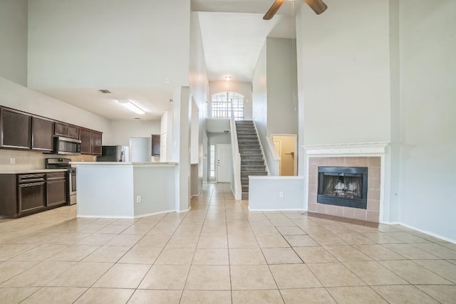 1001 Acanthus St, Pflugerville, TX 78660 - unfurnished living room featuring a high ceiling, light tile patterned flooring, a ceiling fan, a tiled fireplace, and stairs