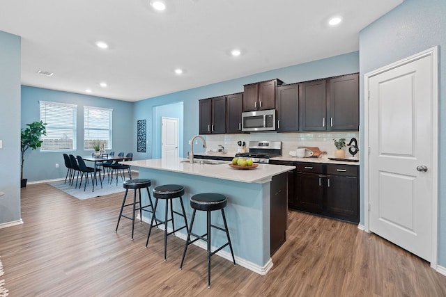 1207 Diggy Dr, Austin, TX 78748 - kitchen with stainless steel appliances, a breakfast bar area, light wood-style flooring, decorative backsplash, and light countertops