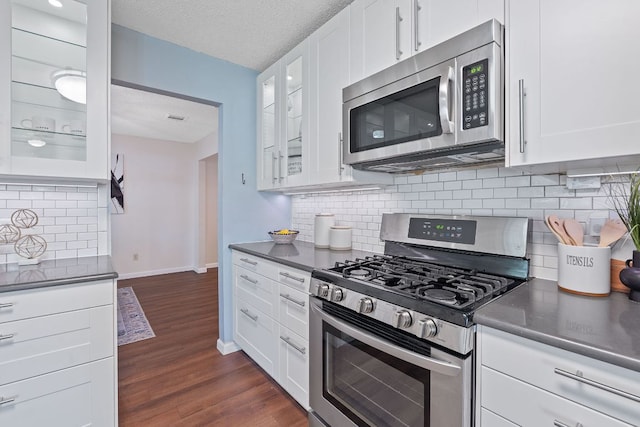 8206 Avocet Dr, Austin, TX 78745 - kitchen featuring stainless steel appliances, dark countertops, white cabinets, dark wood-style floors, and decorative backsplash