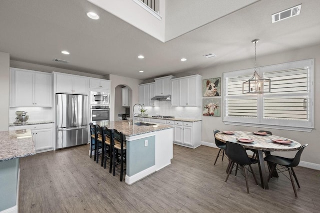 15913 Villa Frontera Dr, Bee Cave, TX 78738 - kitchen featuring stainless steel appliances, arched walkways, wood finished floors, a kitchen breakfast bar, and recessed lighting