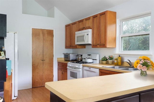 1917 Miles Ave, Austin, TX 78745 - kitchen with white appliances, lofted ceiling, light countertops, brown cabinets, and light wood finished floors