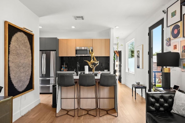 4802 Gladeview Dr Unit 2, Austin, TX 78745 - kitchen featuring appliances with stainless steel finishes, light wood-style flooring, tasteful backsplash, a breakfast bar, and light countertops