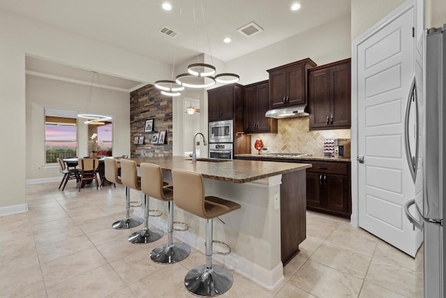 9110 Bayshore Bnd Unit 30, Austin, TX 78726 - kitchen with stainless steel appliances, under cabinet range hood, backsplash, a breakfast bar area, and an island with sink