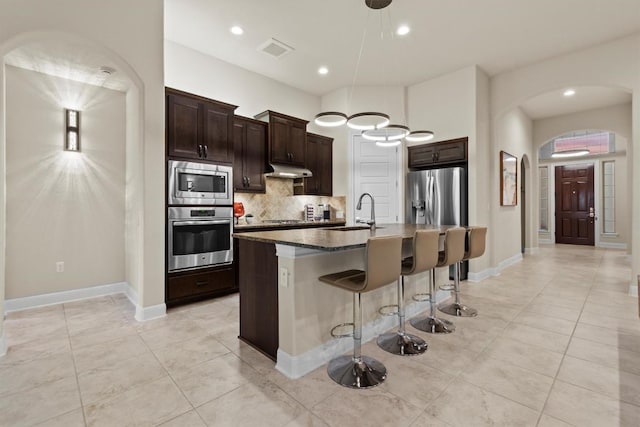 9110 Bayshore Bnd Unit 30, Austin, TX 78726 - kitchen with appliances with stainless steel finishes, arched walkways, decorative backsplash, a breakfast bar area, and light tile patterned flooring