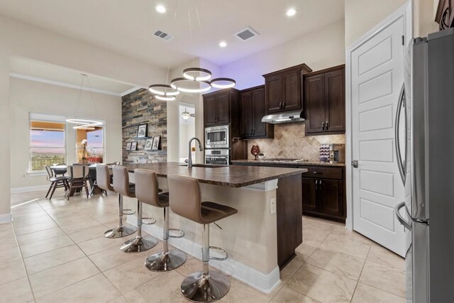 9110 Bayshore Bnd Unit 30, Austin, TX 78726 - kitchen featuring stainless steel appliances, under cabinet range hood, a breakfast bar, backsplash, and dark brown cabinets