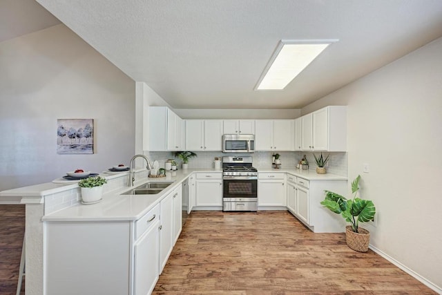 1803 Kwai Cv, Leander, TX 78641 - kitchen with appliances with stainless steel finishes, a peninsula, backsplash, light wood-style flooring, and lofted ceiling