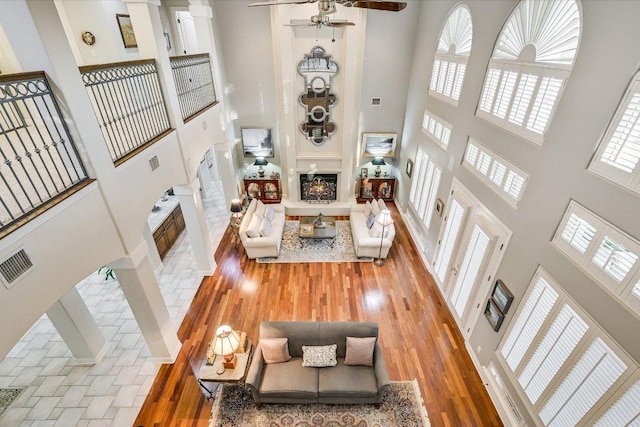 9105 Westminster Glen Ave, Austin, TX 78730 - living room featuring a high ceiling, a lit fireplace, wood finished floors, and a ceiling fan