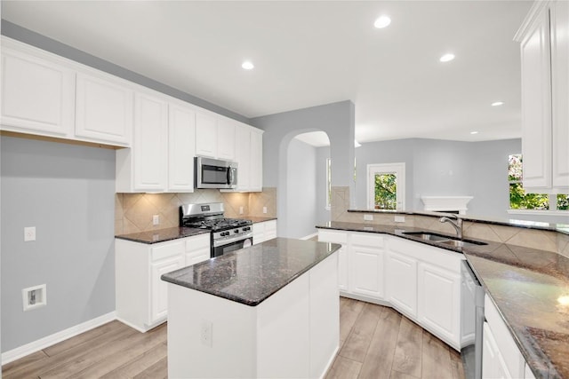 1086 Sussex Way, Round Rock, TX 78665 - kitchen featuring appliances with stainless steel finishes, light wood finished floors, dark stone countertops, arched walkways, and recessed lighting