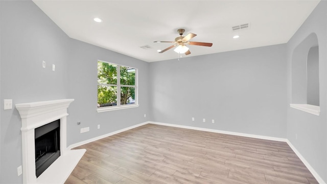 1086 Sussex Way, Round Rock, TX 78665 - unfurnished living room featuring arched walkways, a ceiling fan, wood finished floors, a fireplace with raised hearth, and recessed lighting