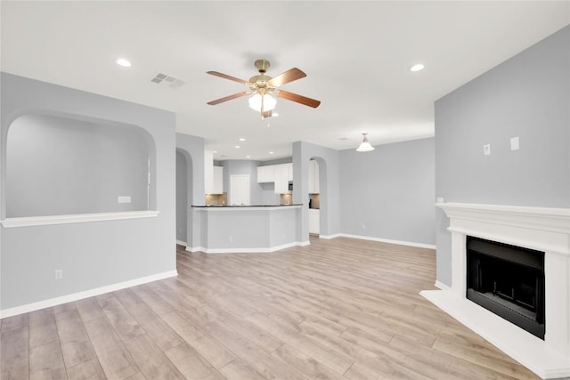 1086 Sussex Way, Round Rock, TX 78665 - unfurnished living room with ceiling fan, arched walkways, light wood-style flooring, a fireplace with raised hearth, and recessed lighting