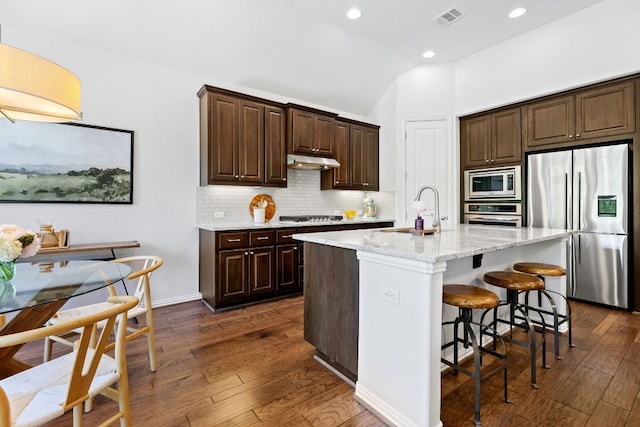 2977 Diego Dr, Round Rock, TX 78665 - kitchen featuring appliances with stainless steel finishes, under cabinet range hood, decorative backsplash, dark brown cabinetry, and dark wood-style floors
