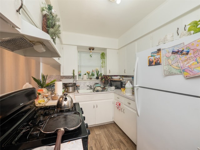 8508 Dryfield Dr, Austin, TX 78758 - kitchen with freestanding refrigerator, black gas range oven, under cabinet range hood, light countertops, and white cabinetry