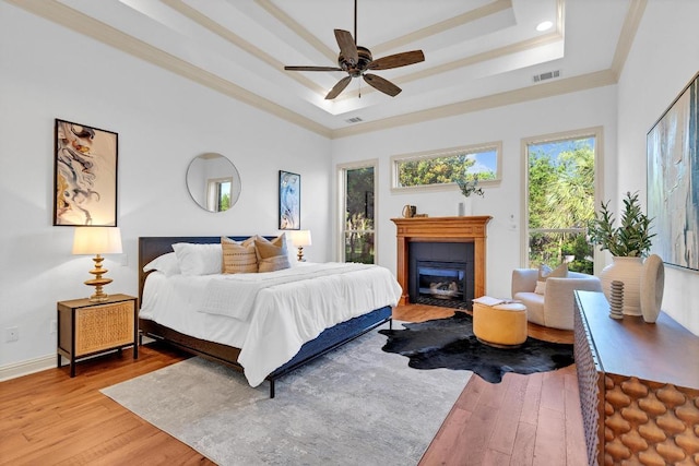 14417 Heron Bay Cv, Bee Cave, TX 78738 - bedroom featuring a tray ceiling, light wood-style floors, a glass covered fireplace, ornamental molding, and a ceiling fan