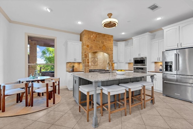 14417 Heron Bay Cv, Bee Cave, TX 78738 - kitchen featuring appliances with stainless steel finishes, backsplash, light stone counters, white cabinets, and a kitchen breakfast bar