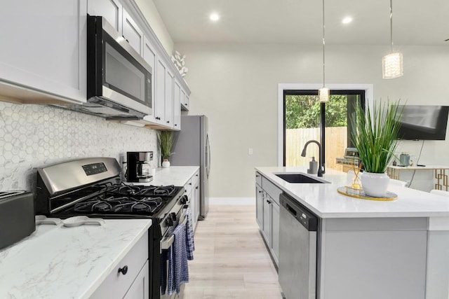 7215 Bennett Ave, Austin, TX 78752 - kitchen with appliances with stainless steel finishes, light wood finished floors, backsplash, a kitchen island with sink, and decorative light fixtures