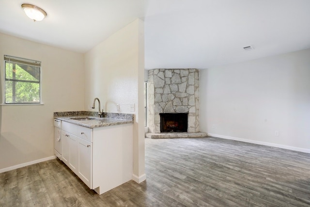 4307 S 1st St Unit 103, Austin, TX 78745 - kitchen with wood finished floors, white cabinetry, light stone countertops, open floor plan, and a stone fireplace