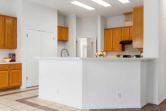4917 Flaming Oak Cv, Austin, TX 78749 - kitchen featuring under cabinet range hood, decorative backsplash, light tile patterned floors, light countertops, and brown cabinets