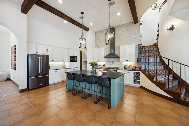 kitchen featuring high end refrigerator, dark countertops, a towering ceiling, beamed ceiling, and decorative backsplash