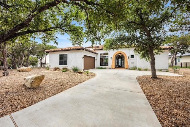 mediterranean / spanish house with an attached garage, driveway, a tile roof, and stucco siding