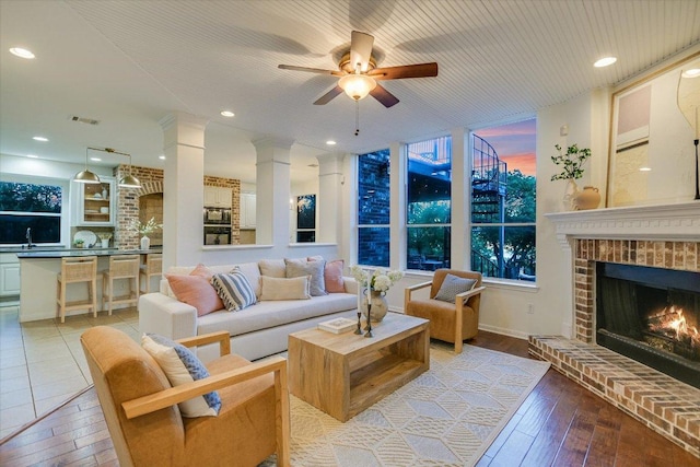 17120 Northlake Hills Dr, Jonestown, TX 78645 - living area with a brick fireplace, ceiling fan, light wood-type flooring, and decorative columns