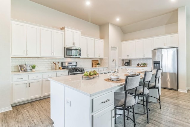 7901 Sunrise Ravine Pass, Lago Vista, TX 78645 - kitchen featuring appliances with stainless steel finishes, a kitchen island with sink, white cabinetry, a breakfast bar area, and decorative backsplash