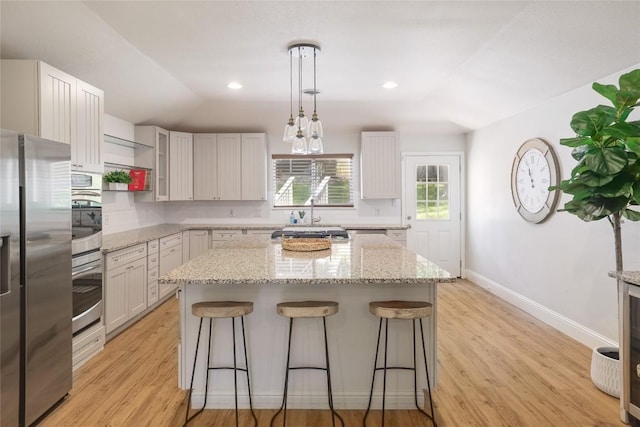 2119 Rabb Rd, Austin, TX 78704 - kitchen with stainless steel appliances, a breakfast bar, a kitchen island, light wood-type flooring, and light stone countertops